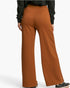 A person shown from the back wearing wide-leg rust-colored pants, a black long-sleeve top, and black sneakers against a clean white studio background.