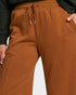 Close-up of a person wearing rust-brown drawstring sweatpants with a black top, showing the waistband, drawstrings, side pocket, and hand.