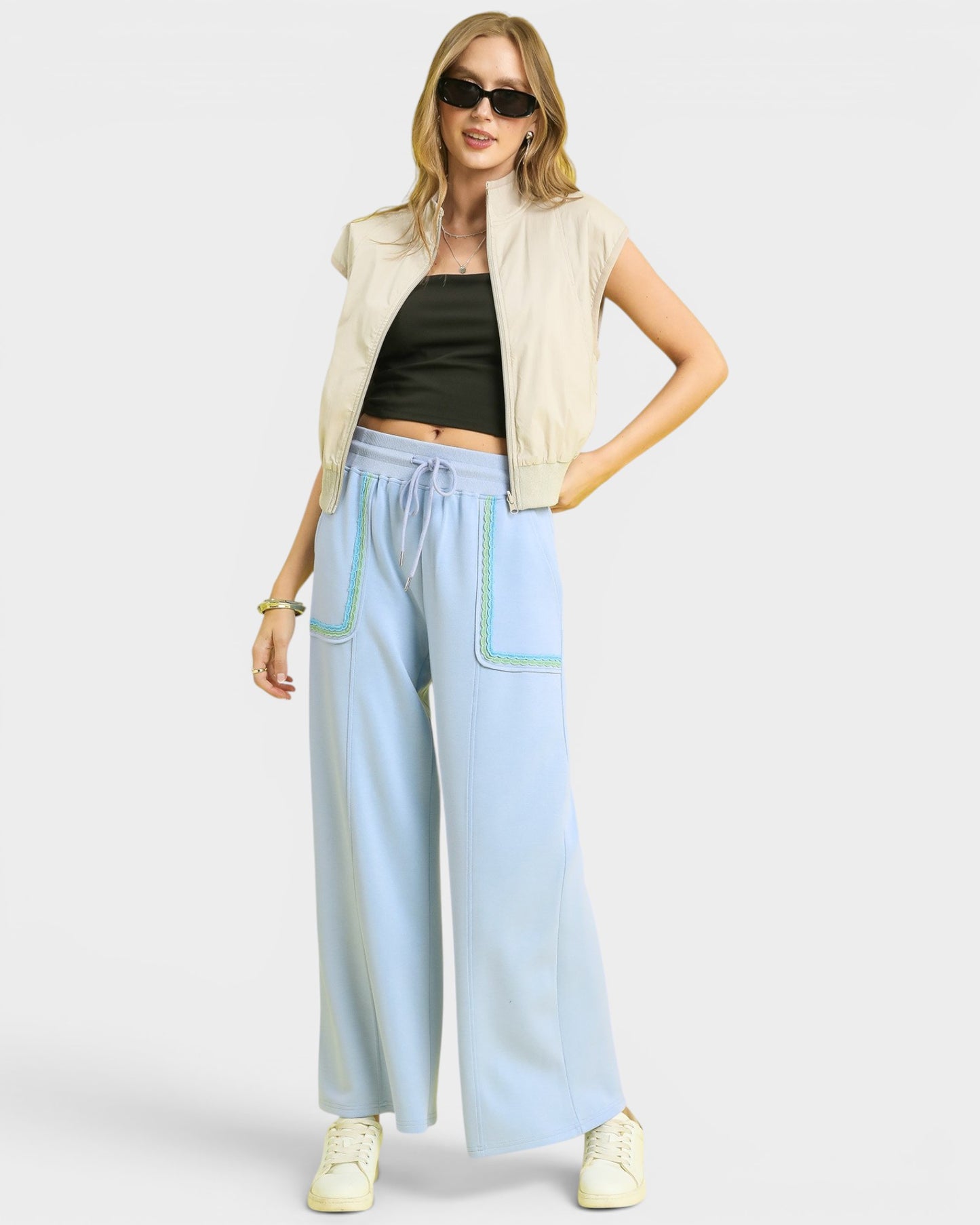 Woman wearing a beige sleeveless jacket, black top, and light blue pants on a white background