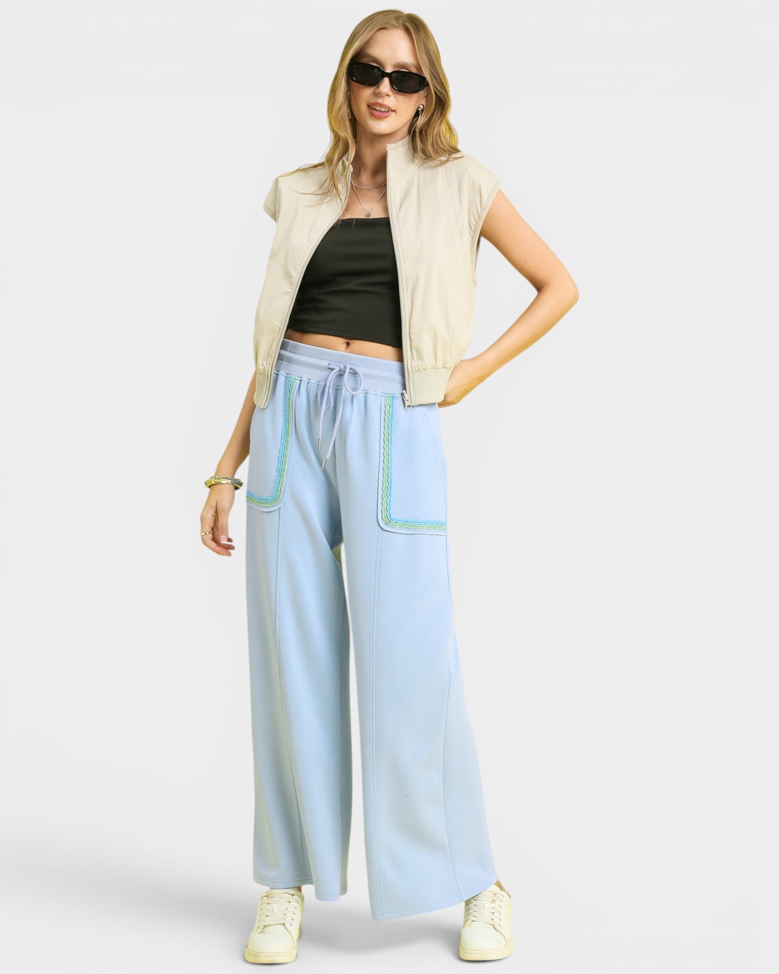 Woman wearing a beige sleeveless jacket, black top, and light blue pants on a white background