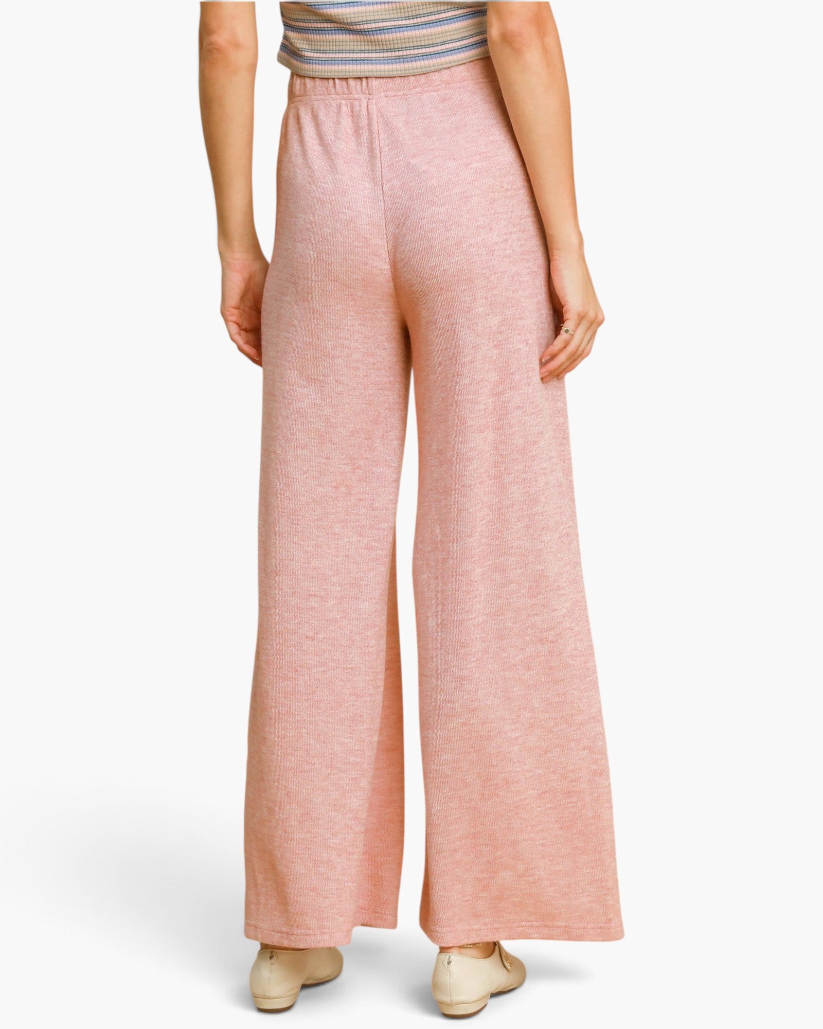 A person shown from the back wearing wide-leg dusty pink pants and a striped top, standing against a clean white studio background.