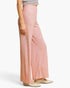 A model wearing a pair of high-waisted, wide-leg knit pants in a heathered dusty pink color, paired with a striped top and beige flats, shown from the waist down against a plain white background.