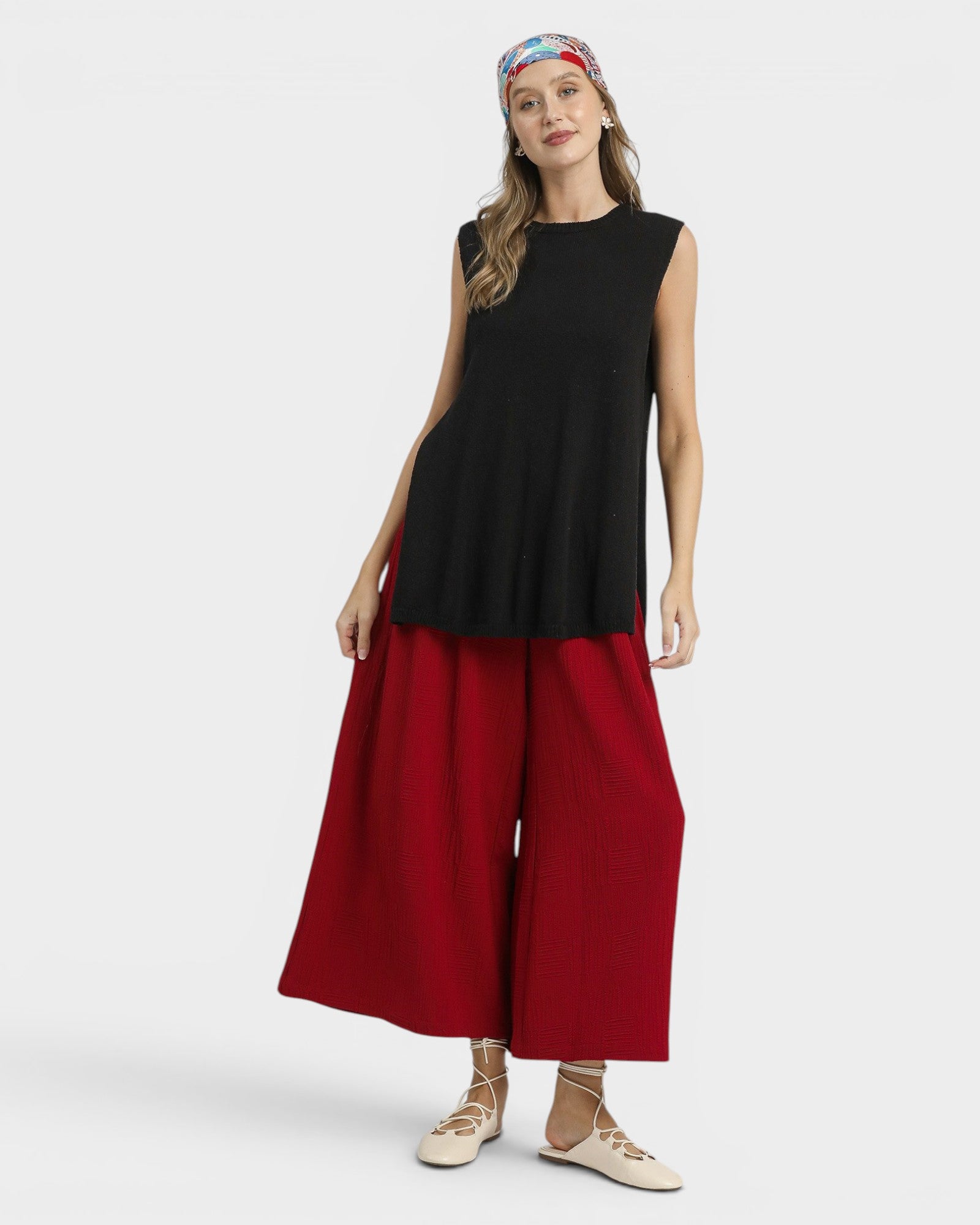 Woman wearing a black sleeveless top and red wide-leg pants on a white background
