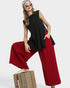 Woman wearing a black sleeveless top and red pants sitting on a wooden crate against a white background.