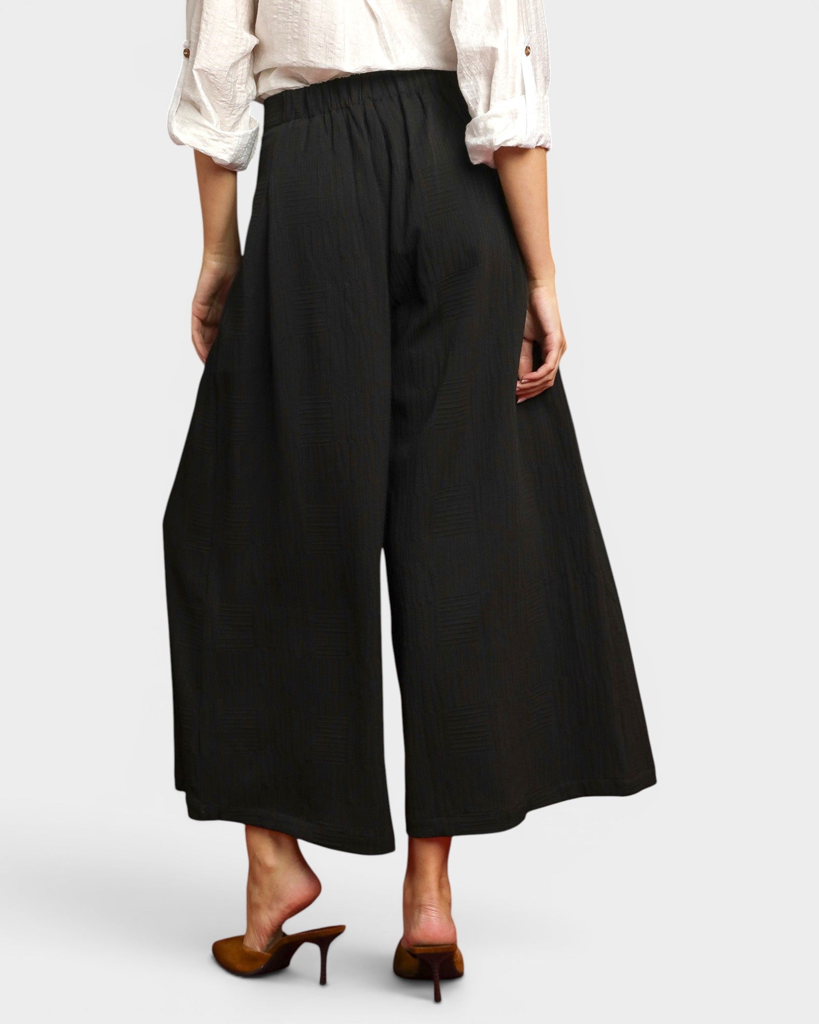 Person wearing black wide-leg pants with a white top on a light gray background