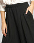 Black pleated skirt worn with a white blouse on a plain background