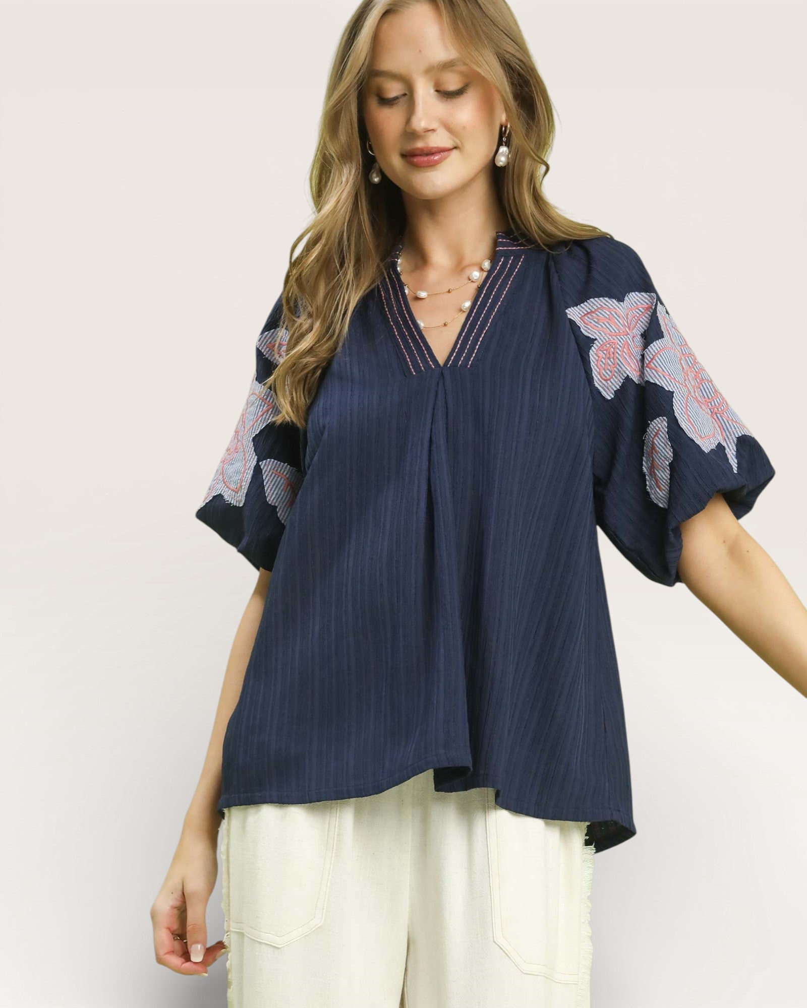 Woman wearing a navy blue blouse with floral sleeves on a plain background