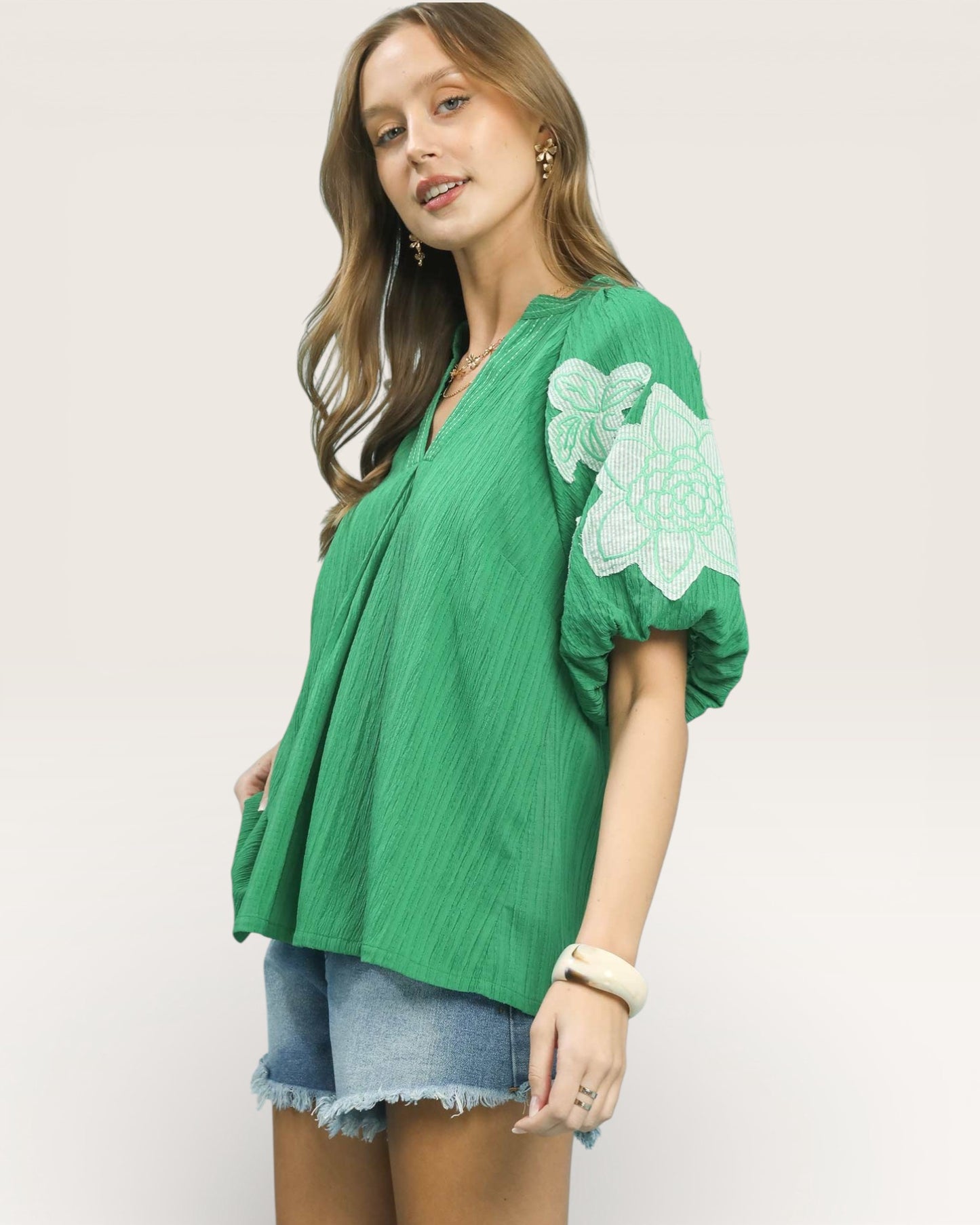 Woman wearing a green top with white embroidery on a plain background