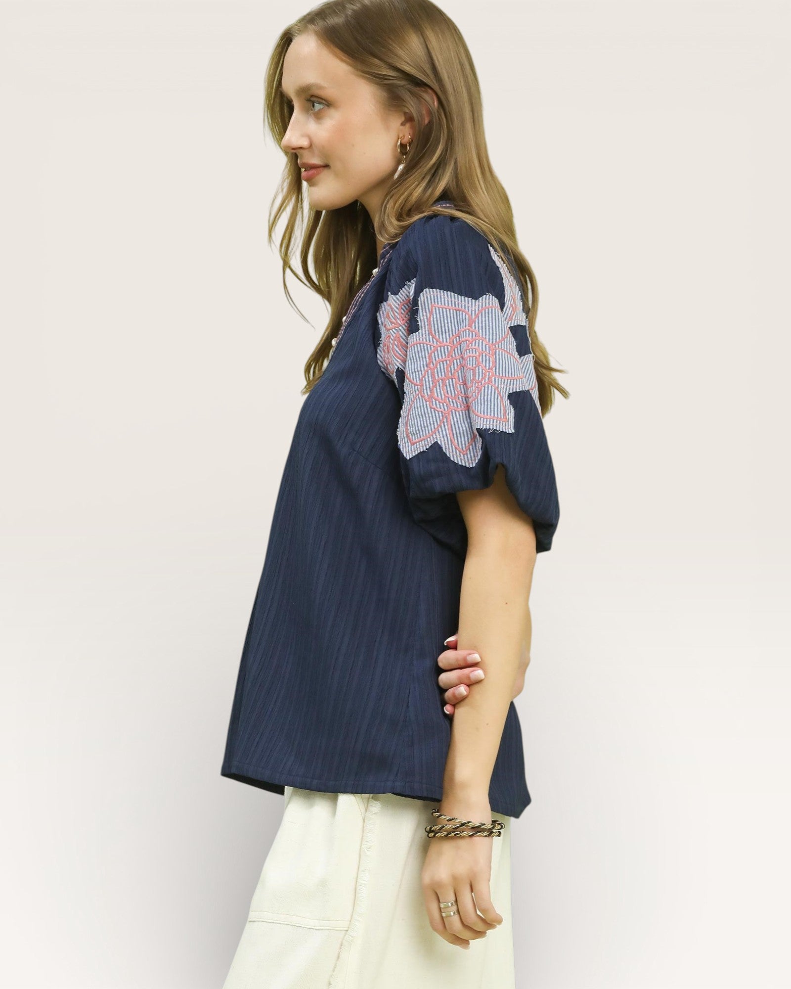 Woman wearing a navy blue top with floral embroidery on a plain background