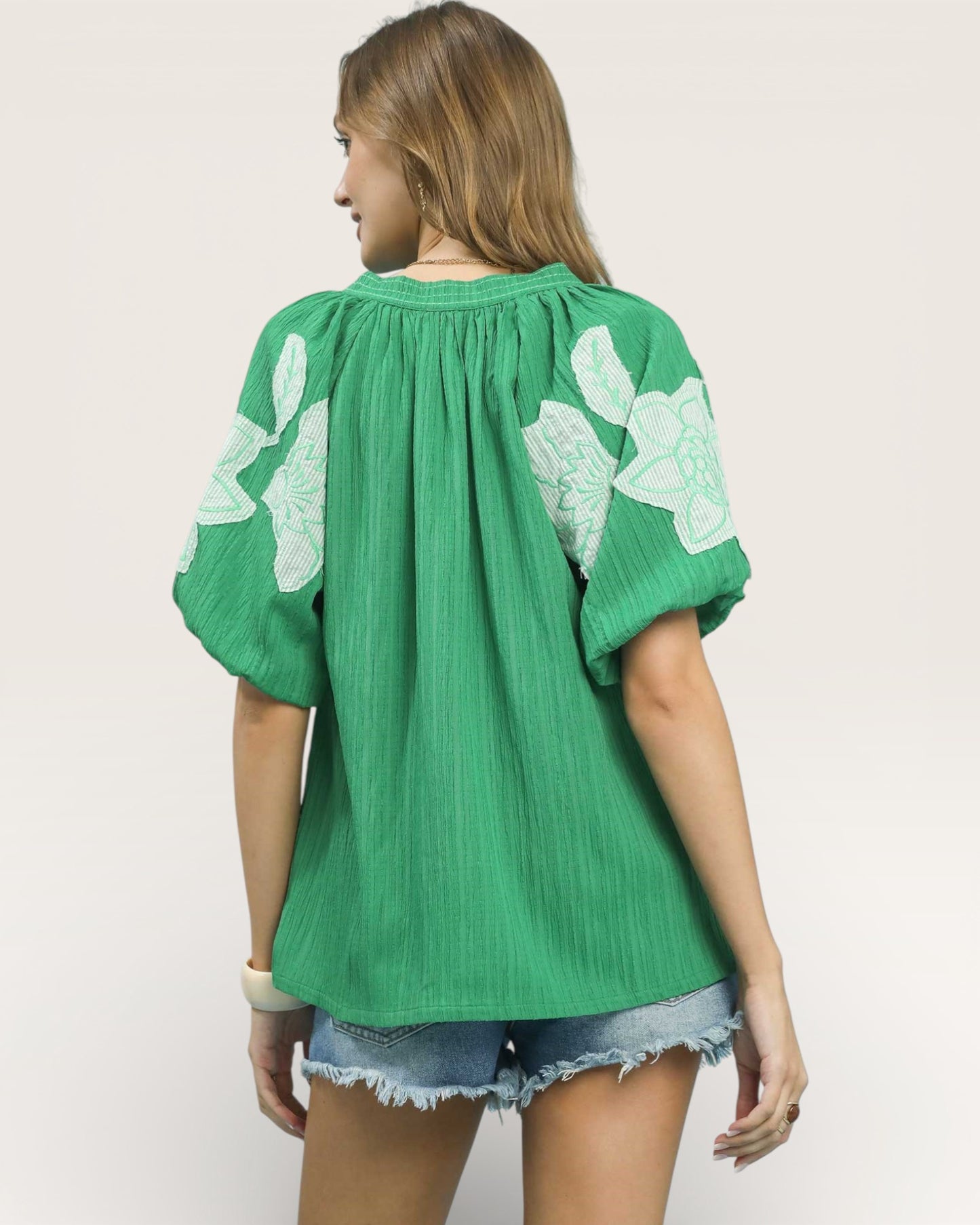 Green blouse with floral patterns on sleeves worn by a person on a plain background