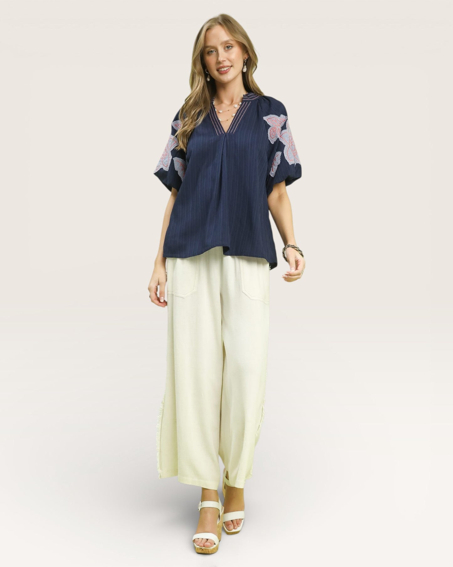 Woman wearing a navy blouse with floral sleeves and light yellow pants on a white background