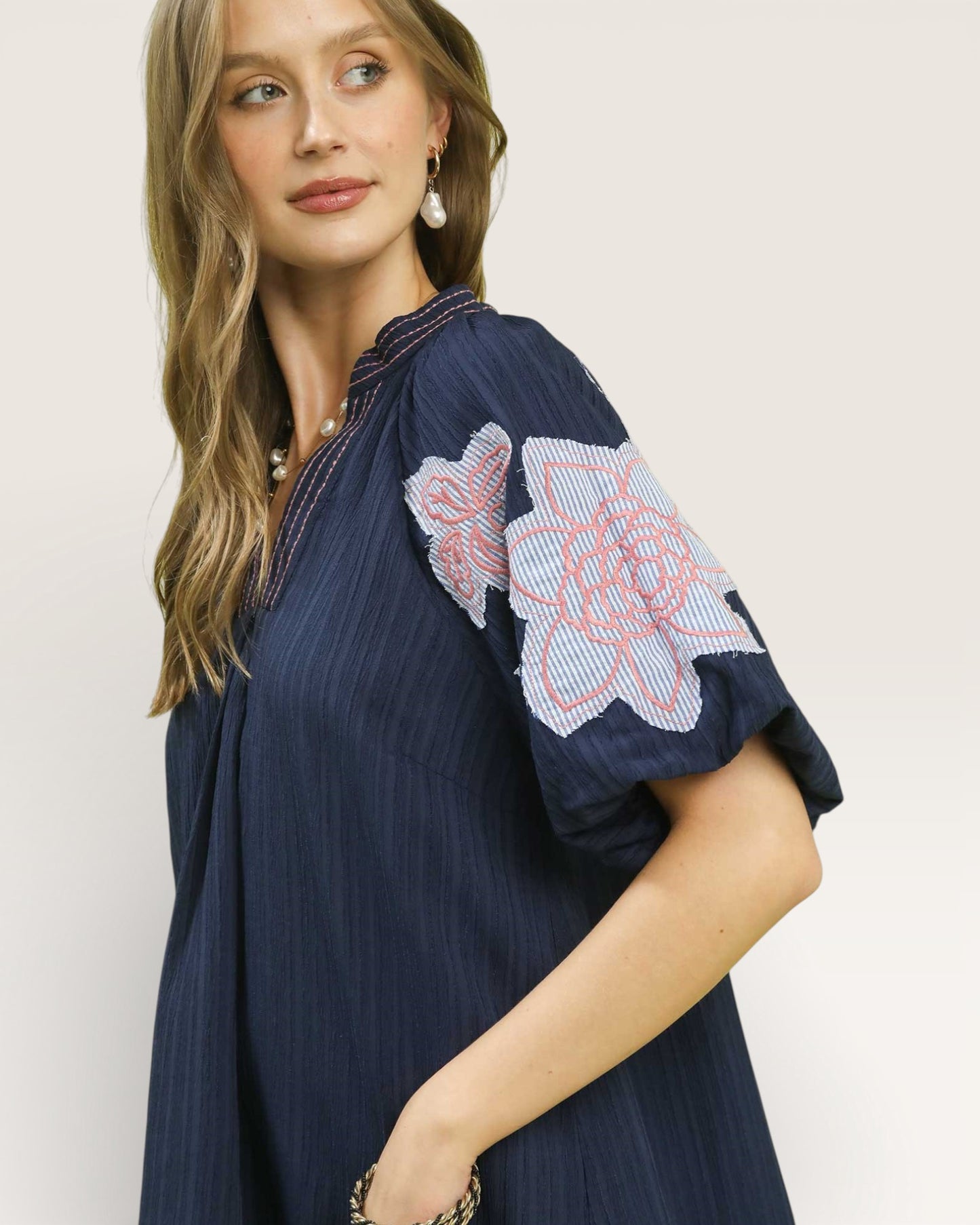 Woman wearing a navy dress with floral embroidery on a plain background