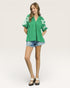 Woman wearing a green blouse with white patterns and denim shorts on a beige background