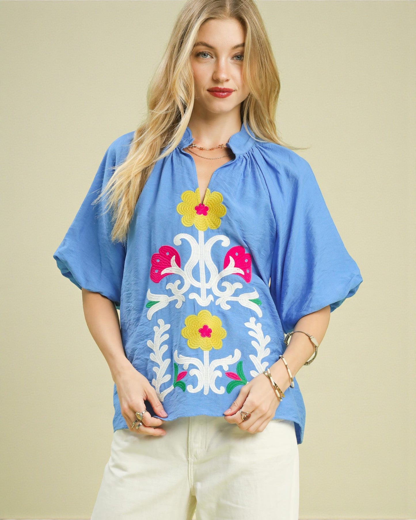 Woman wearing a blue blouse with floral embroidery on a beige background