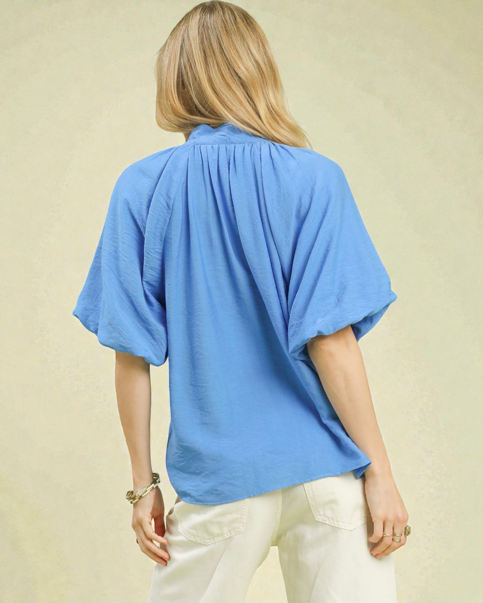 Person wearing a blue top and white pants on a beige background