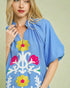 Woman wearing a blue dress with colorful floral embroidery on a beige background