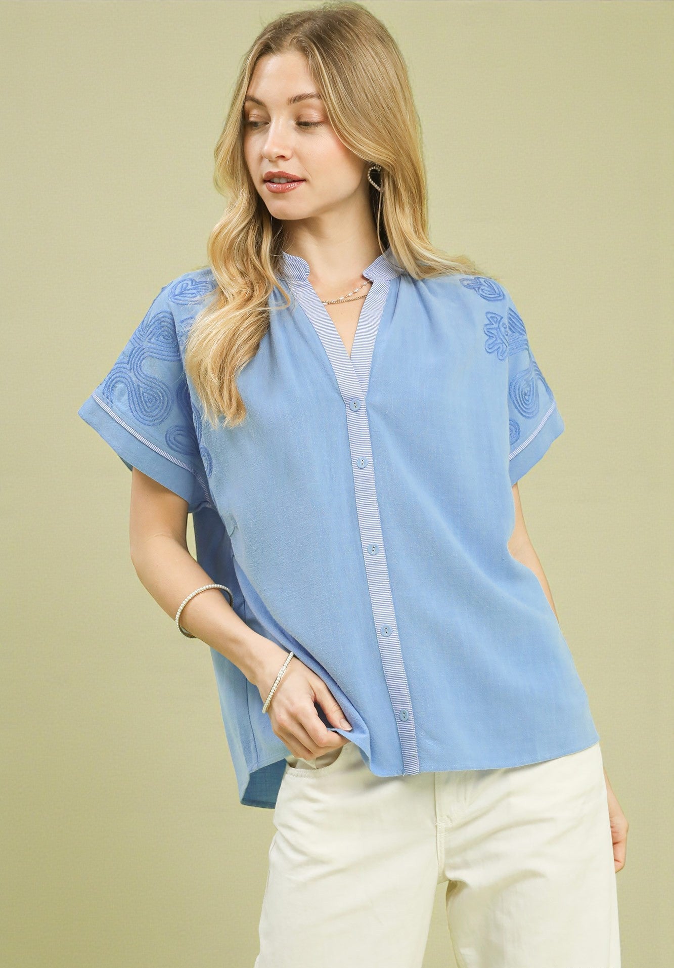 Woman wearing a light blue blouse with lace details on a beige background