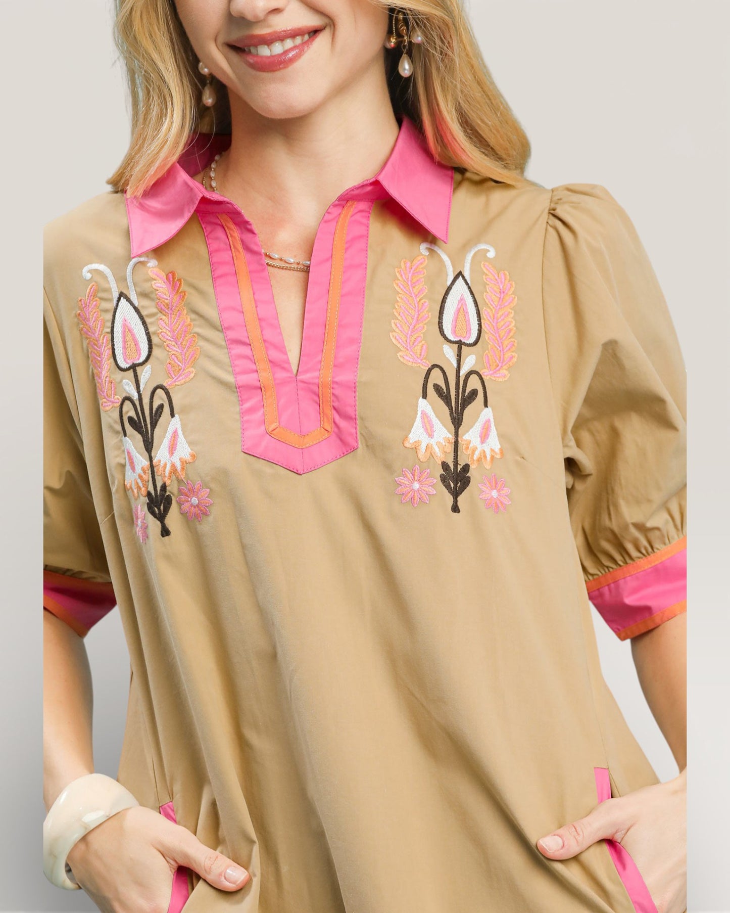 Beige blouse with pink and black embroidery on a plain background