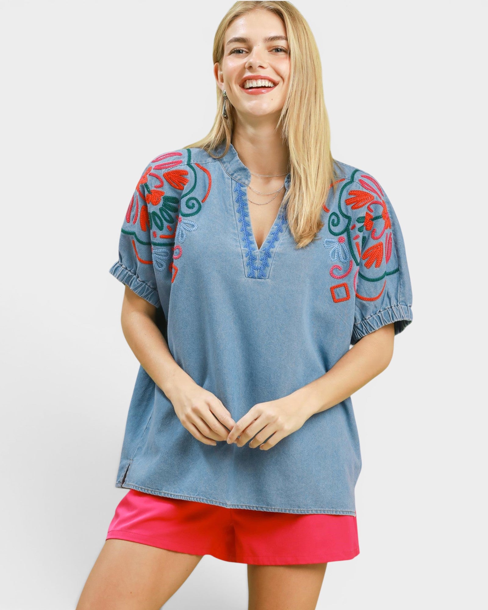 Woman wearing a blue denim top with colorful floral embroidery on a white background