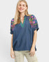 Woman wearing a blue denim blouse with colorful embroidery on a white background