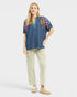 Woman wearing a blue embroidered top and beige pants on a white background