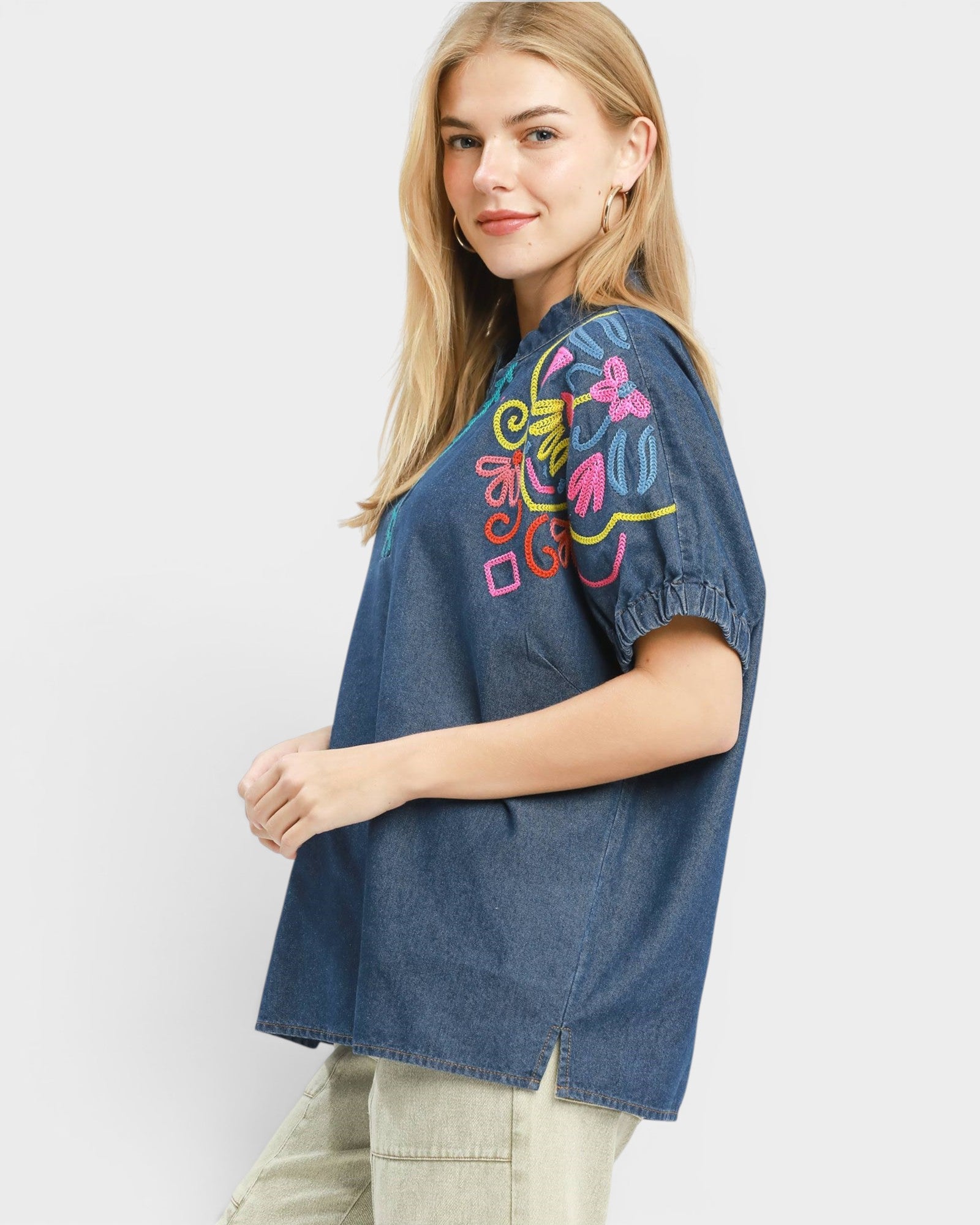 Woman wearing a denim shirt with colorful embroidery on a white background