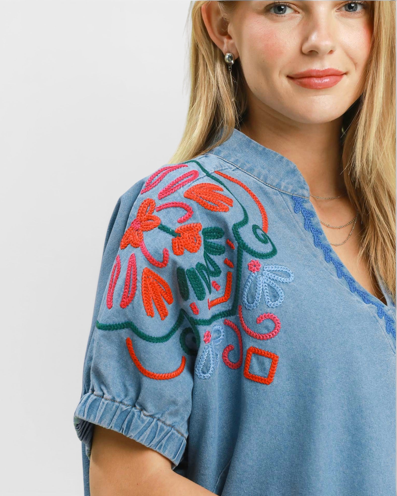 Woman wearing a denim shirt with colorful floral embroidery on a plain background