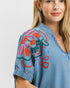 Woman wearing a denim shirt with colorful floral embroidery on a plain background