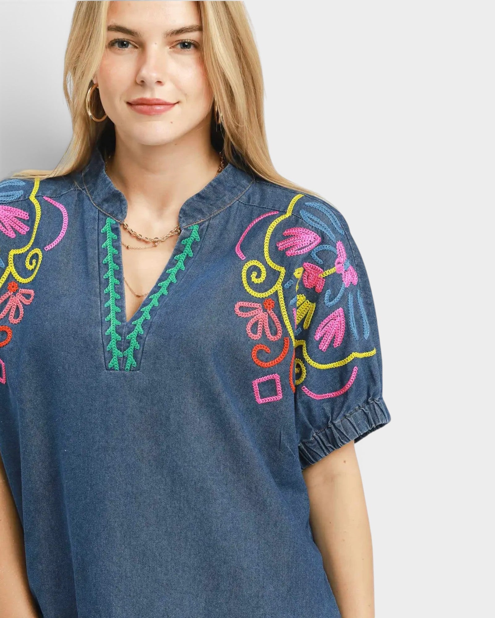 Woman wearing a blue denim blouse with colorful embroidery on a plain background