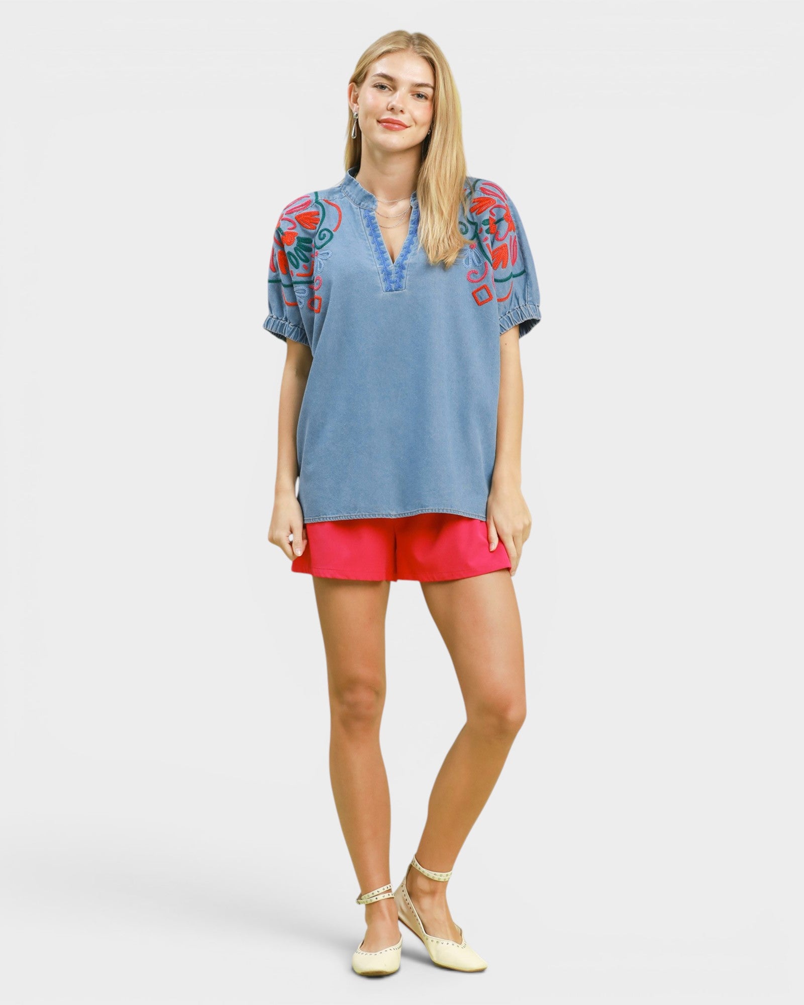 Woman wearing a blue embroidered top and pink shorts on a white background