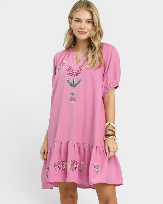 Woman wearing a pink dress with floral embroidery on a white background