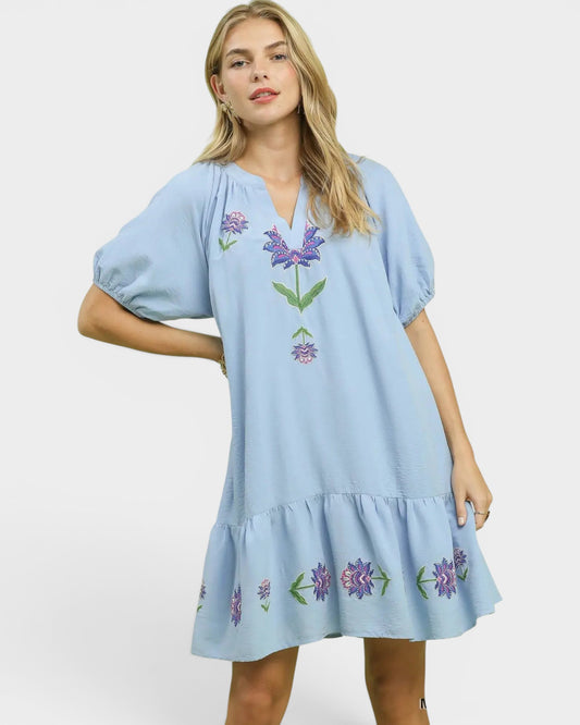 Woman wearing a light blue dress with floral embroidery on a white background