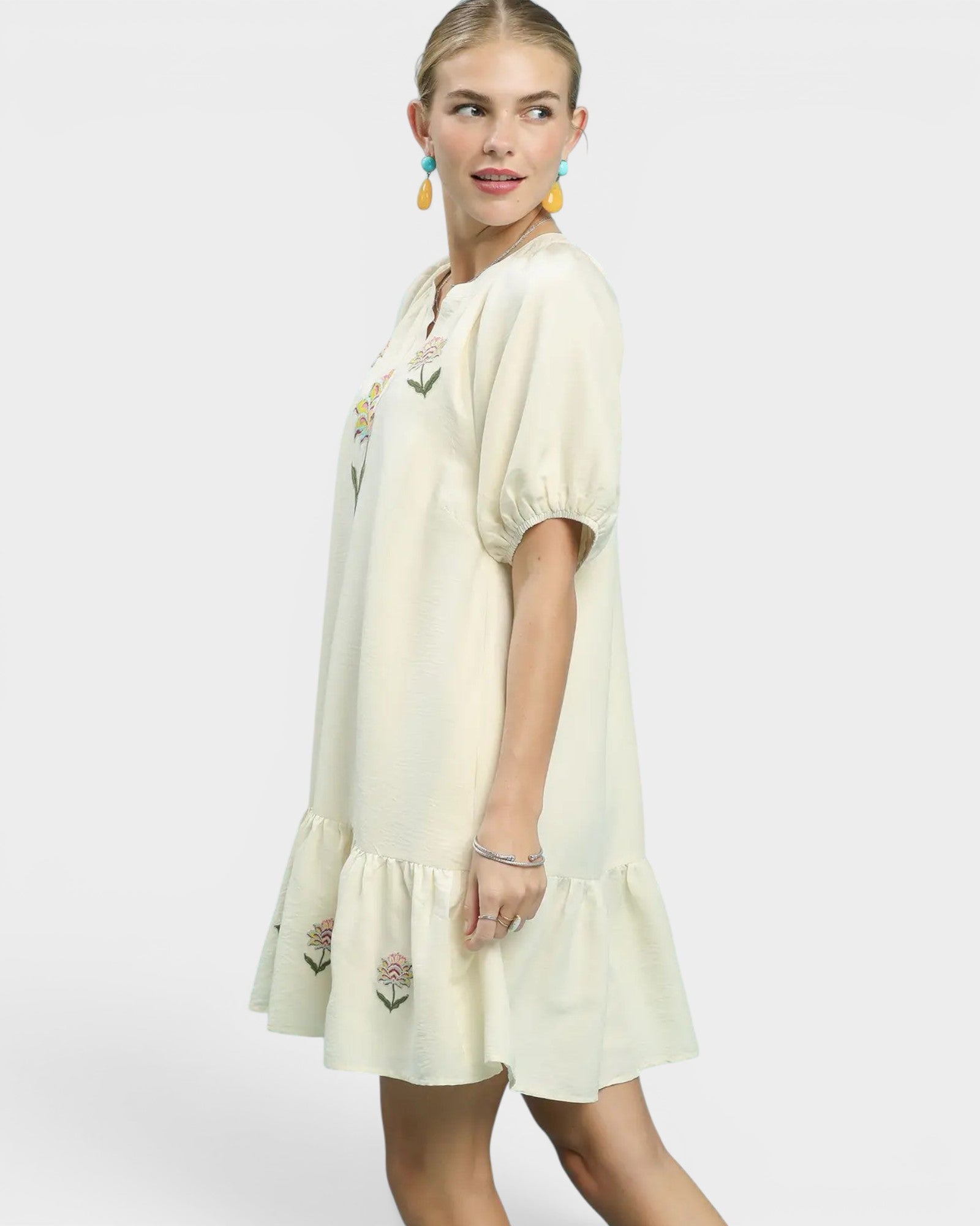 Woman wearing a cream-colored dress with embroidery on a white background