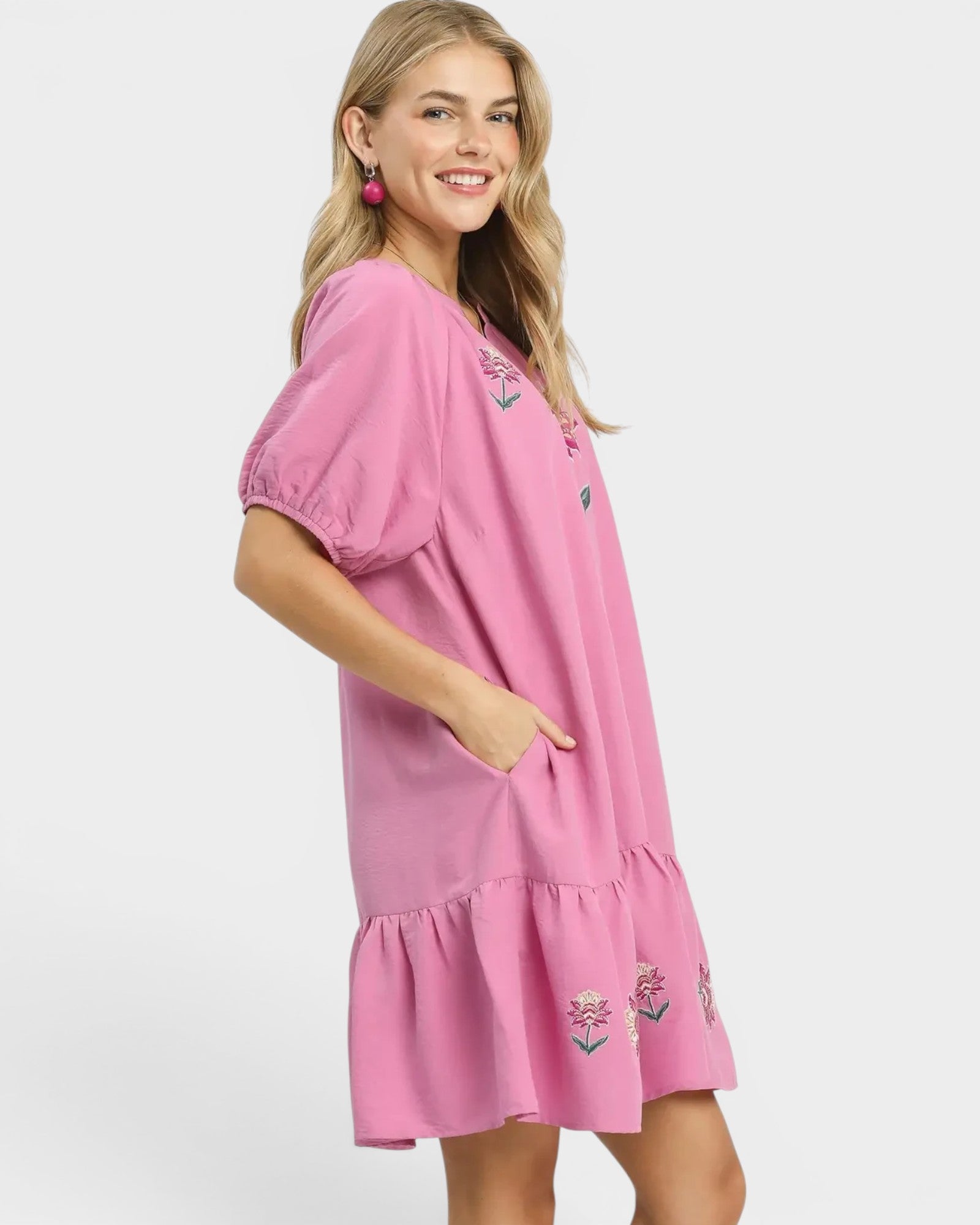 Woman wearing a pink dress with floral embroidery on a white background