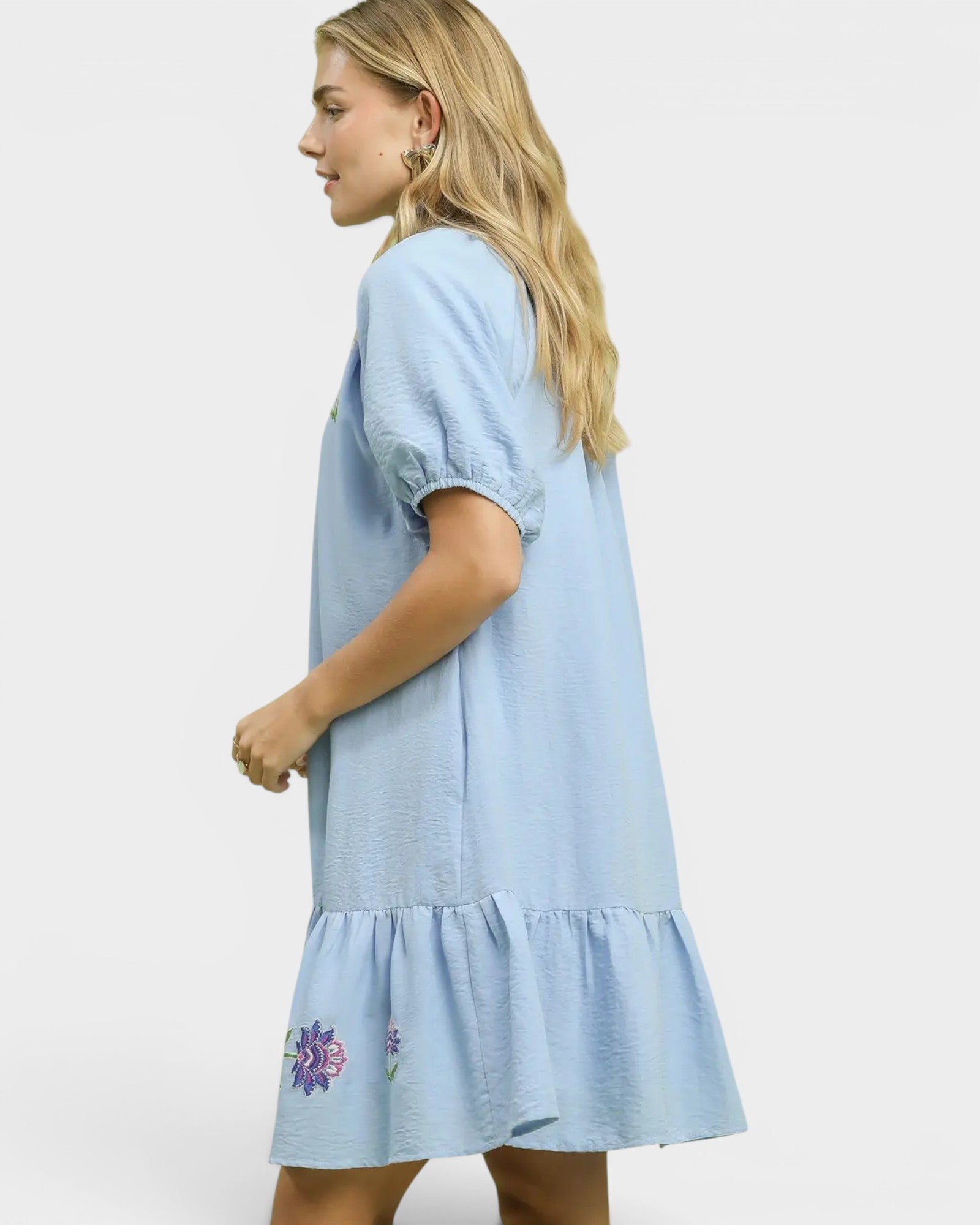 Woman wearing a light blue dress with floral embroidery on a white background