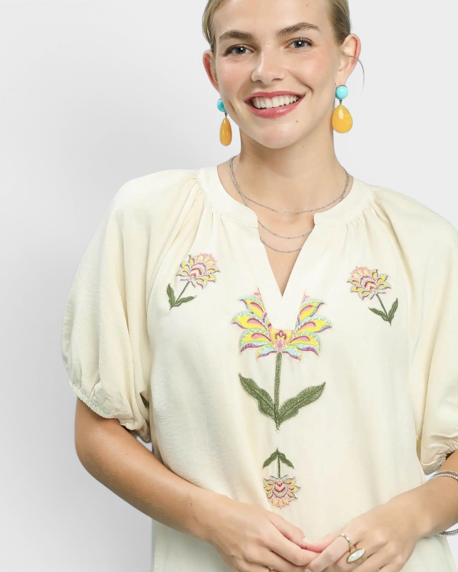 Woman wearing a cream-colored blouse with floral embroidery on a plain background