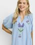 Woman wearing a light blue embroidered blouse with floral designs on a plain background