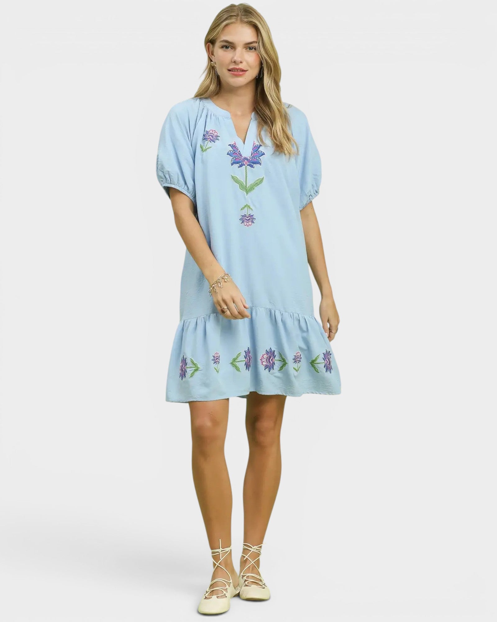 Woman wearing a light blue dress with floral embroidery on a white background