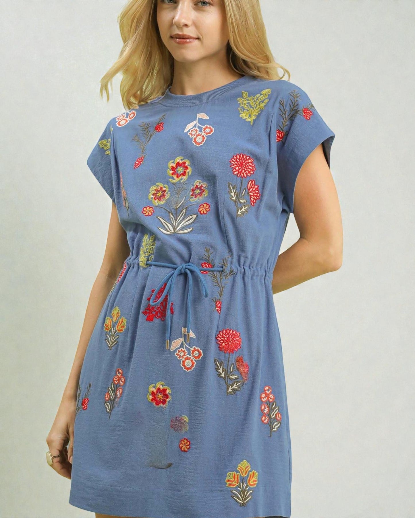Woman wearing a blue dress with colorful floral embroidery on a plain background