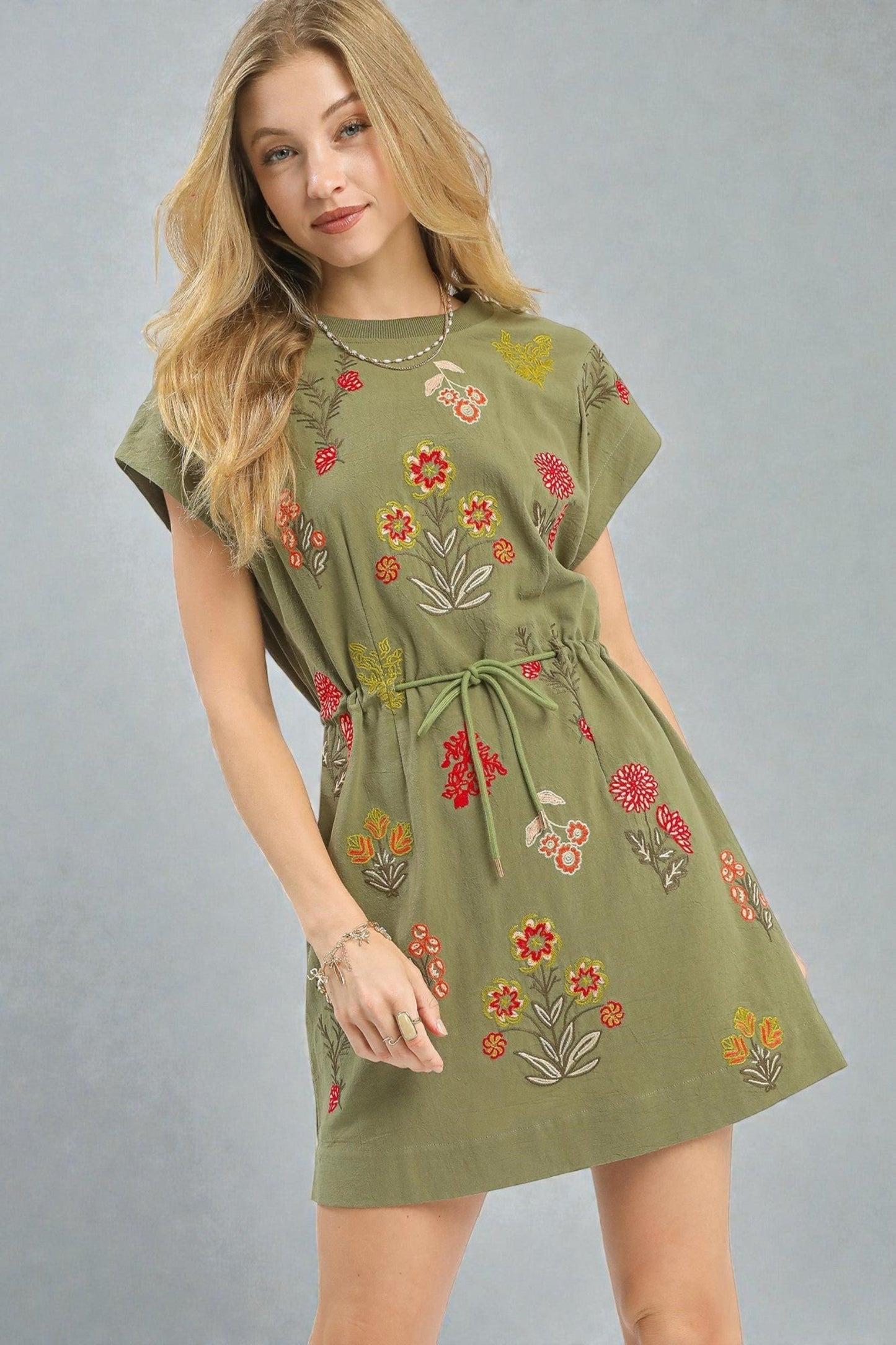 Woman wearing a green dress with floral embroidery on a gray background