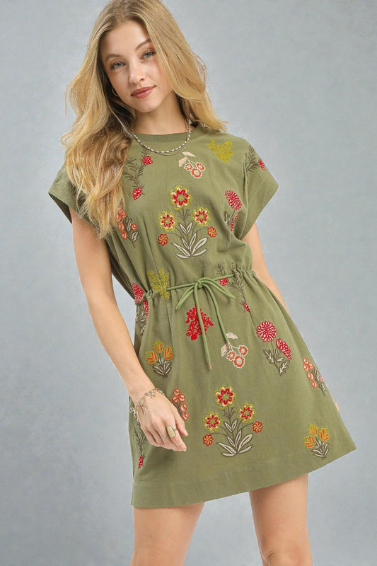 Woman wearing a green dress with floral embroidery on a gray background