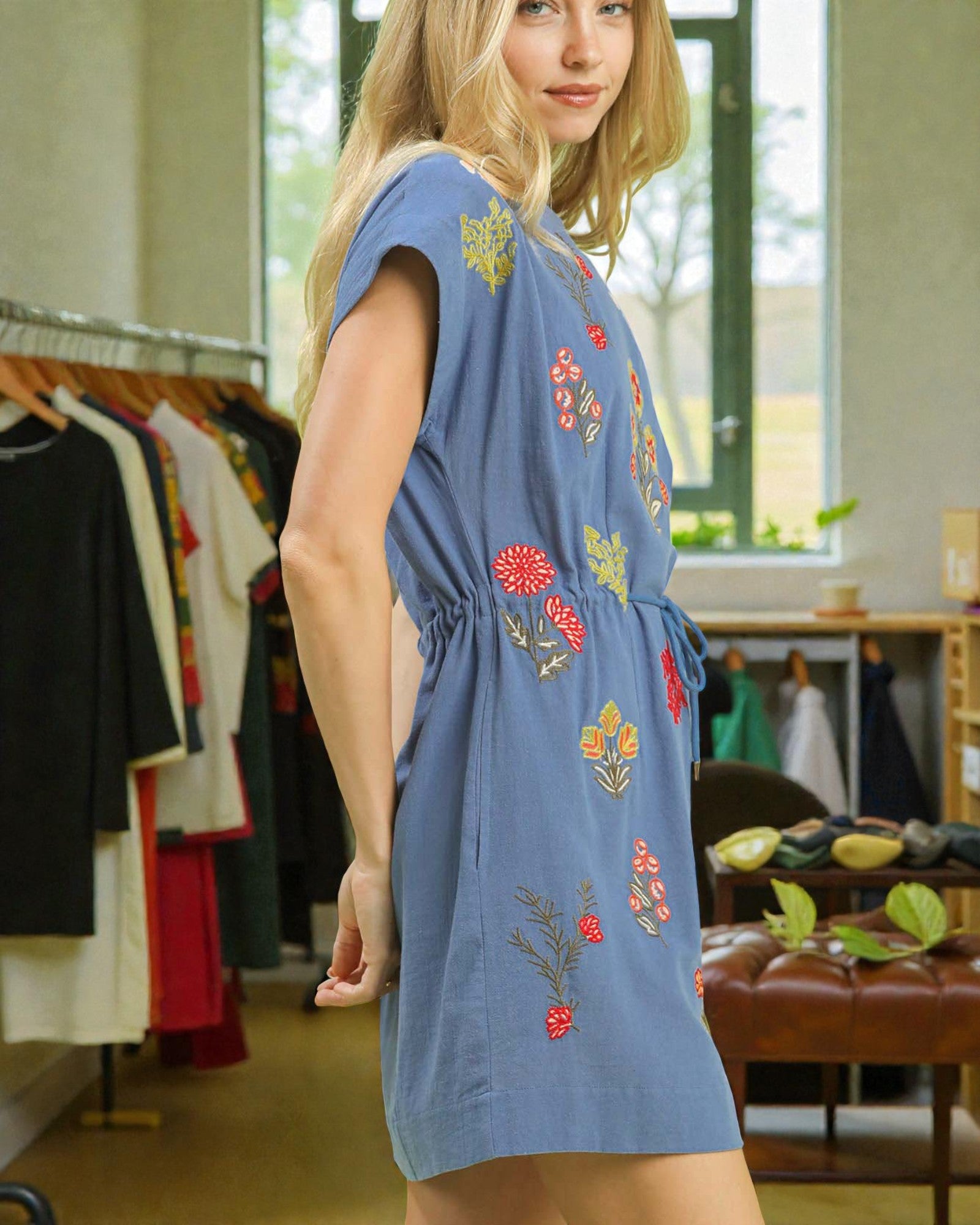 Woman wearing a blue dress with floral embroidery in a clothing store.
