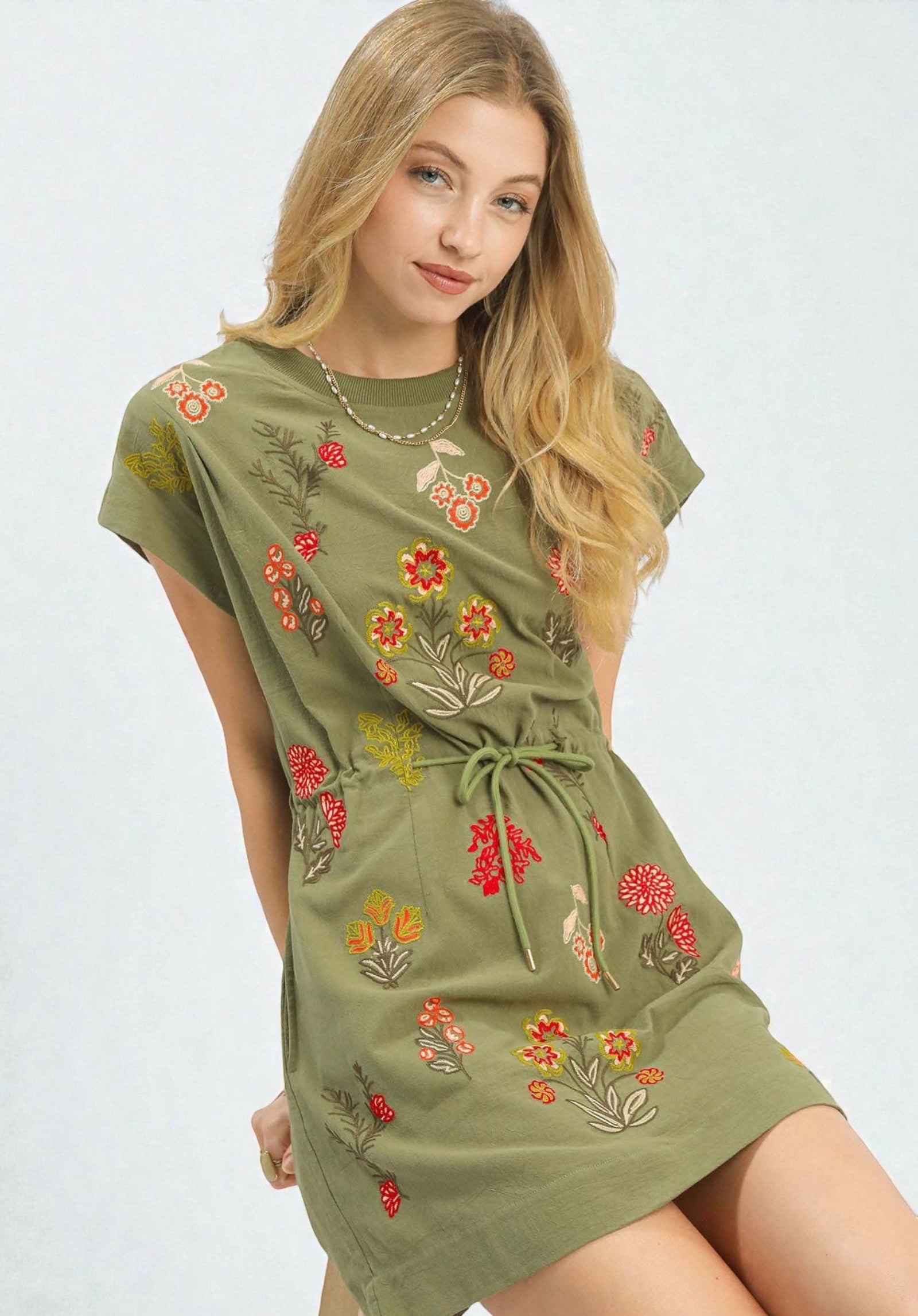 Woman wearing a green dress with floral embroidery on a white background