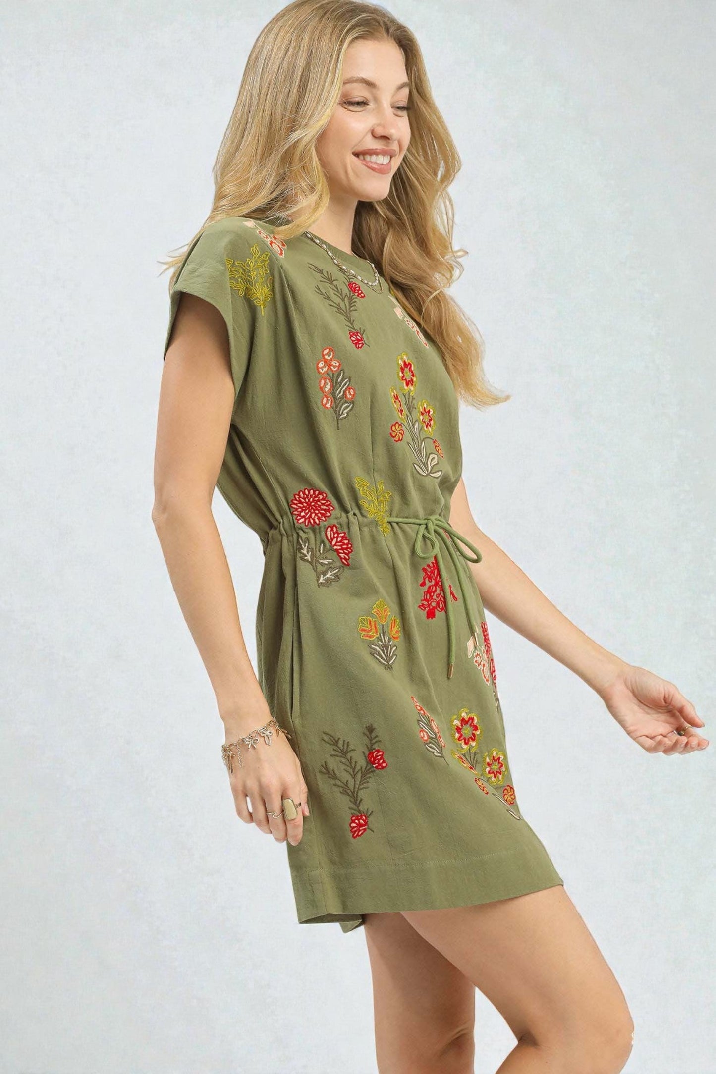 Woman wearing a green dress with floral embroidery on a white background