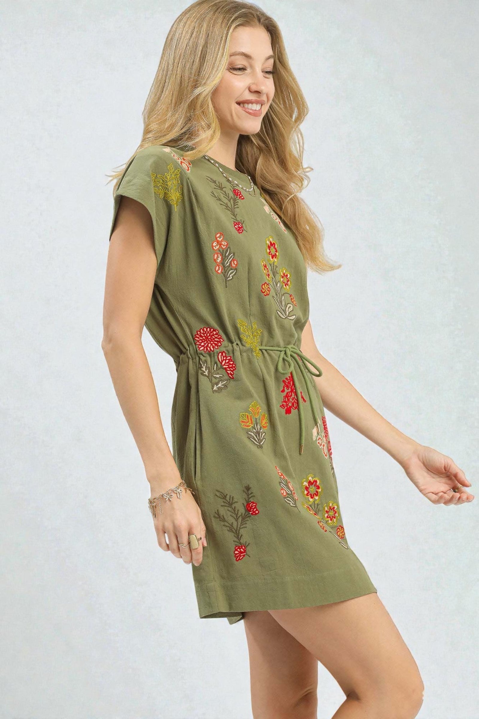 Woman wearing a green dress with floral embroidery on a white background