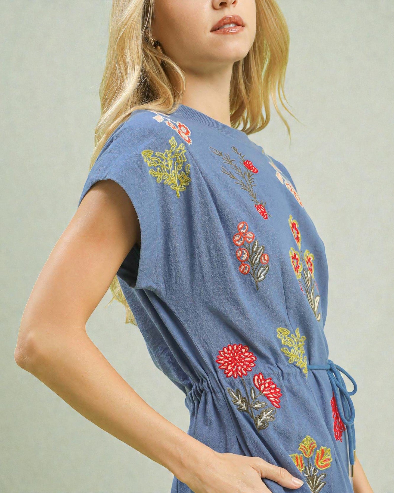 Woman wearing a blue dress with floral embroidery on a plain background