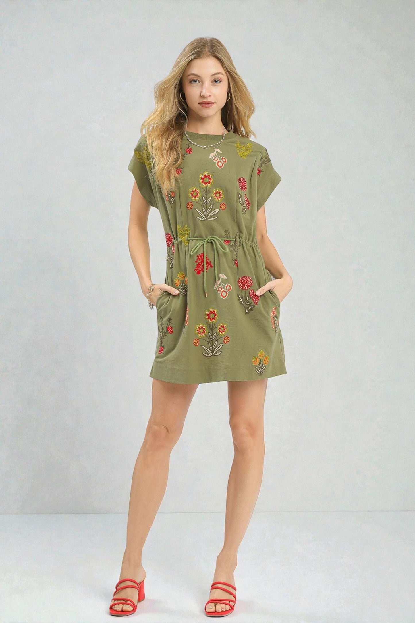 Woman wearing a green dress with floral embroidery on a plain background