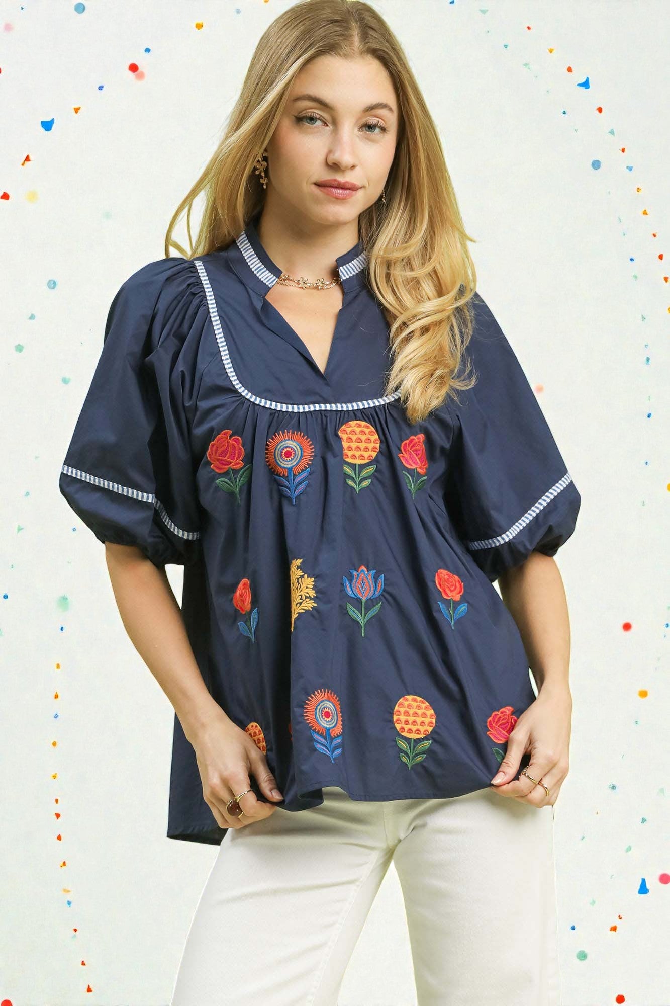 Woman wearing a navy blue blouse with colorful floral embroidery against a multicolored dot patterned background
