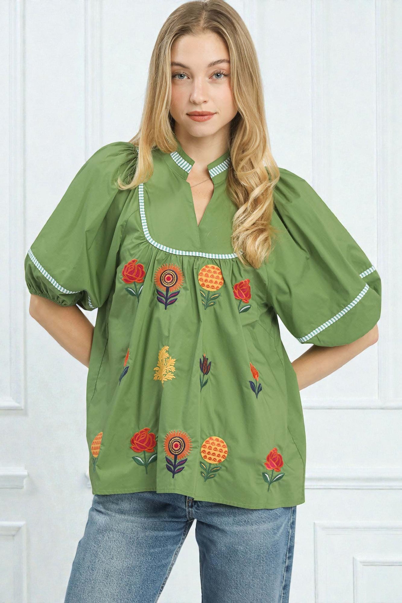 Woman wearing a green embroidered blouse with floral patterns against a white background
