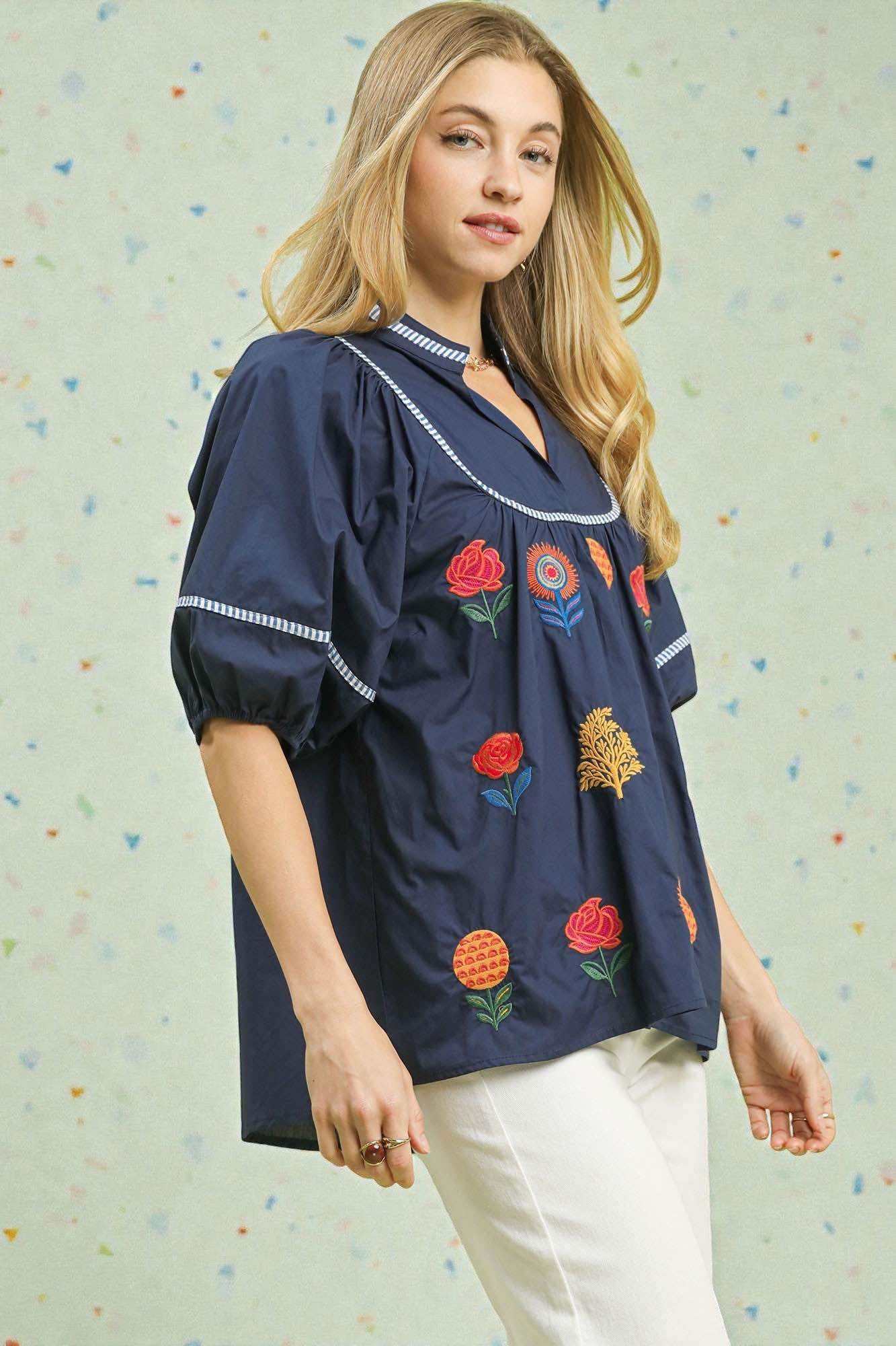 Woman wearing a navy blue blouse with colorful embroidery against a light background